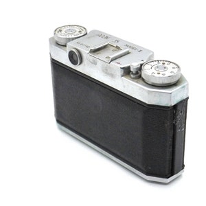 Pu&ograve; includere: Una macchina fotografica a pellicola da 35 mm argentata e nera con un rivestimento in pelle nera. La macchina fotografica ha un obiettivo argentato e un quadrante argentato sul lato destro. La macchina fotografica ha il testo "ALPA" e "Model-1" sulla parte superiore.