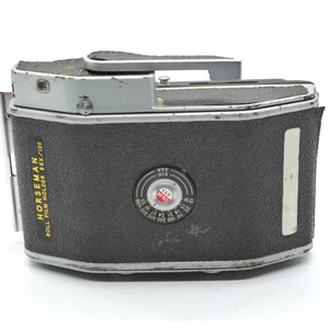 Puede incluir: Un porta rollo de pel&iacute;cula Horseman negro y plateado para pel&iacute;cula 6x/120. El porta rollo tiene una ventana circular con un logotipo "Kodak" rojo y un dial blanco y negro con marcas para diferentes velocidades de pel&iacute;cula.