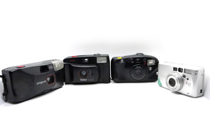 Puede incluir: Cuatro c&aacute;maras de pel&iacute;cula compactas diferentes, incluyendo una Argus negra, una Vivitar negra, una Minolta Zoom Plus negra y una Ziss plateada.
