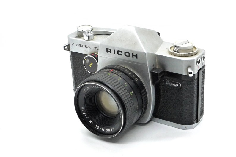 May include: A silver and black Ricoh Singleflex TL camera with a black lens that reads "Lens Made in Japan Auto Rikenon 50mm f1.9".