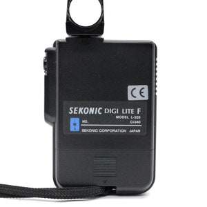 May include: A black Sekonic Digi Lite F light meter with a model number L-328 and C=340. The light meter has a small, round, white light sensor on top and a black strap attached to the bottom.