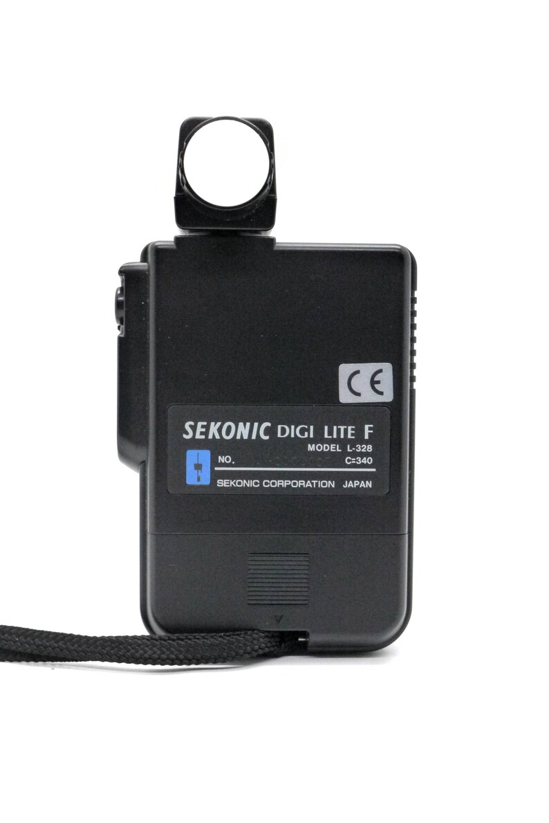 May include: A black Sekonic Digi Lite F light meter with a model number L-328 and C=340. The light meter has a small, round, white light sensor on top and a black strap attached to the bottom.