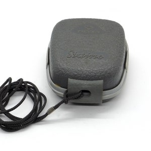 Puede incluir: Una caja rectangular gris texturizada con la palabra "Sixims" impresa en ella. La caja tiene un cord&oacute;n negro adjunto.