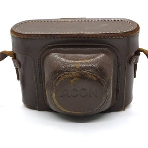 Pu&ograve; includere: Un astuccio per fotocamera in pelle marrone con una tracolla e la scritta "ACON" in rilievo sul davanti.