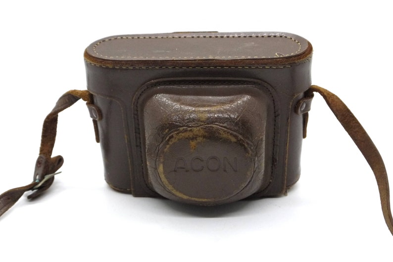 Pu&ograve; includere: Un astuccio per fotocamera in pelle marrone con una tracolla e la scritta "ACON" in rilievo sul davanti.