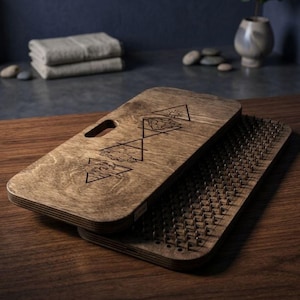 May include: A rectangular wooden sadhu board with a handle cutout, featuring four laser-engraved triangular symbols representing elements. The bottom board is covered in a dense grid of sharp metal nails for standing, while the top board acts as a lid.