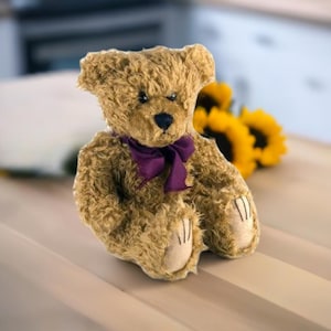 May include: A soft teddy bear with light brown fur, a dark purple bow, and a black nose. The bear has beige paws and is placed in front of yellow sunflowers.