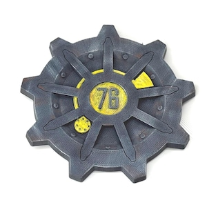 Op de afbeelding: Een grijs en geel cirkelvormig embleem met een tandwielachtig ontwerp. Het midden toont het nummer "76" in geel. Het embleem heeft een verweerde, metalen uitstraling, wat wijst op een vintage of industrieel thema.