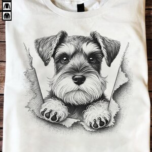 May include: White t-shirt with a black and white Schnauzer dog illustration. The dog appears to be breaking through the fabric. The design showcases the dog's face and paws. The t-shirt has a crew neck.