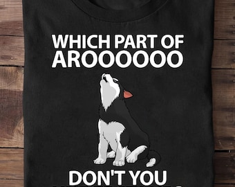 May include: Black t-shirt featuring a howling wolf illustration. The text reads "WHICH PART OF AROOOOO DON'T YOU UNDERSTAND?" The wolf is depicted in black, white, and gray with red ear accents. The shirt is folded on a wooden surface.