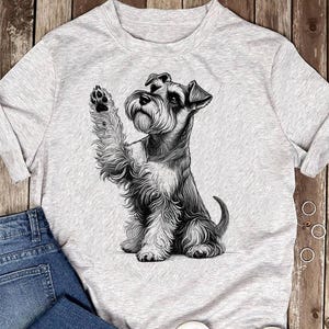 Könnte beinhalten: Ein hellgrau meliertes T-Shirt mit einer detaillierten schwarz-weißen Skizze eines sitzenden Schnauzers, der eine Pfote hebt. Der Hund hat ein zotteliges Fell, spitze Ohren und einen markanten Bart, dargestellt in einem realistischen Stil.