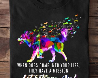 May include: Black t-shirt featuring a colorful dog design with a rainbow of colors. The dog is surrounded by dandelion seeds with small dog silhouettes. The text reads, "WHEN DOGS COME INTO YOUR LIFE, THEY HAVE A MISSION Let Them In!"