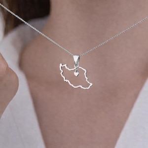 May include: A silver pendant necklace. The pendant is shaped like a country's outline, with a small heart charm. The necklace hangs from a fine chain. The necklace is worn around the neck.