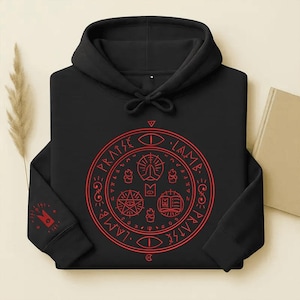 May include: Black hooded sweatshirt with a red circular graphic on the front and a smaller graphic on the left sleeve. The graphic on the front features the words "Praise Lame" around a central design with symbols. The sweatshirt has a drawstring hood.