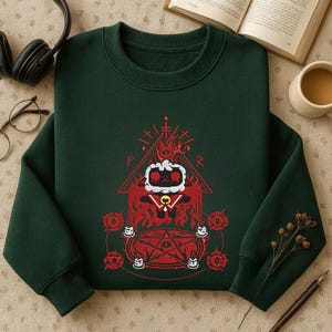 May include: Dark green sweatshirt featuring a red graphic design with a pentagram, flames, and a central character. The design is surrounded by symbols and shapes. The sweatshirt is made of a soft material.