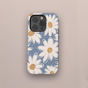 Peut inclure: Une coque de téléphone avec un motif de marguerites. La coque a un fond bleu clair avec des marguerites blanches et des centres jaunes. Le motif est répété sur la surface de la coque.