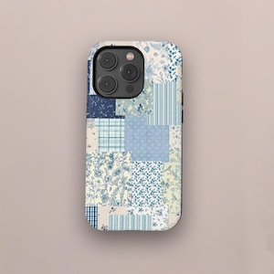 Op de afbeelding: Een telefoonhoesje met een patchwork-ontwerp in blauwe en crèmetinten. De hoes heeft een verscheidenheid aan patronen, waaronder bloemenprints, strepen en ruiten. De hoes heeft een camera-uitsparing en knoppen.