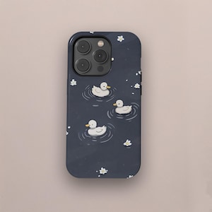 May include: A navy blue phone case with a charming illustration of three white ducks on a pond. White flowers are scattered around the ducks. The case has a glossy finish and a protective design.
