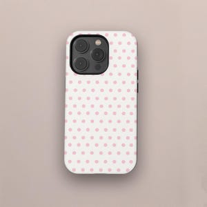 Op de afbeelding: Een witte telefoonhoes met een herhalend patroon van kleine, gelijkmatig verdeelde roze stippen. De hoes heeft een camera-uitsparing met drie lenzen en een flitser. De telefoonhoes is effen van kleur en heeft een gladde textuur.