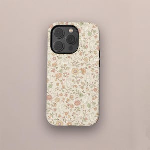 Puede incluir: Una funda de teléfono con un estampado floral y de conejos. La funda presenta un fondo color crema con un diseño repetido de conejos blancos, flores rosas, naranjas y verdes, y hojas verdes. La funda tiene un módulo de cámara negro.