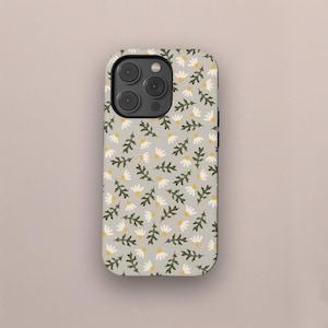 May include: A phone case with a floral pattern. The case features a light gray background covered in small white daisy-like flowers with yellow centers and dark green leaves. The case has a camera cutout.