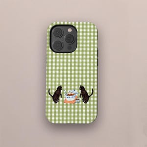 May include: A phone case featuring a green and white gingham pattern. The case has a watercolor illustration of two black cats facing each other near a pot of food and a cup. The case has a camera and flash.
