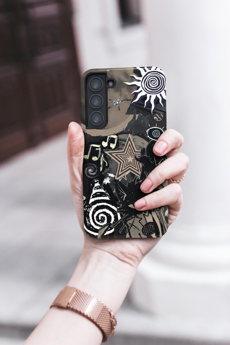 Puede incluir: Una funda de tel&eacute;fono negra y marr&oacute;n con un dise&ntilde;o &uacute;nico que presenta un sol, estrellas, notas musicales y formas abstractas. La funda se sostiene en una mano, mostrando la intrincada obra de arte y la matriz de la c&aacute;mara del tel&eacute;fono.