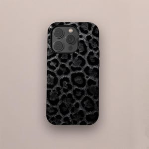 Könnte beinhalten: Eine Handyhülle mit schwarzem und grauem Leopardenmuster. Die Hülle hat eine glänzende Oberfläche und weist ein Muster aus dunkelgrauen Flecken auf schwarzem Hintergrund auf. Die Handyhülle hat einen Kameraausschnitt mit drei Linsen.