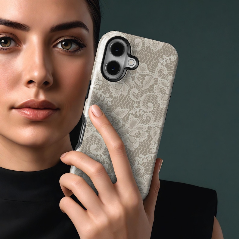 May include: A smartphone case with a beige and white lace pattern. The case has a black border and a camera cutout. The lace design is intricate and detailed, creating a delicate and elegant look. The case is held in a person's hand.