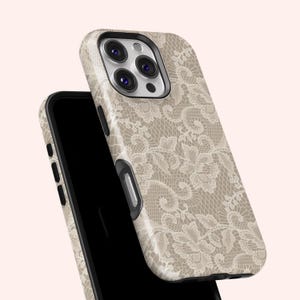 May include: A beige phone case with a delicate, off-white lace pattern. The case is shown on top of a black smartphone, with the camera lenses visible. The design is a floral lace overlay.