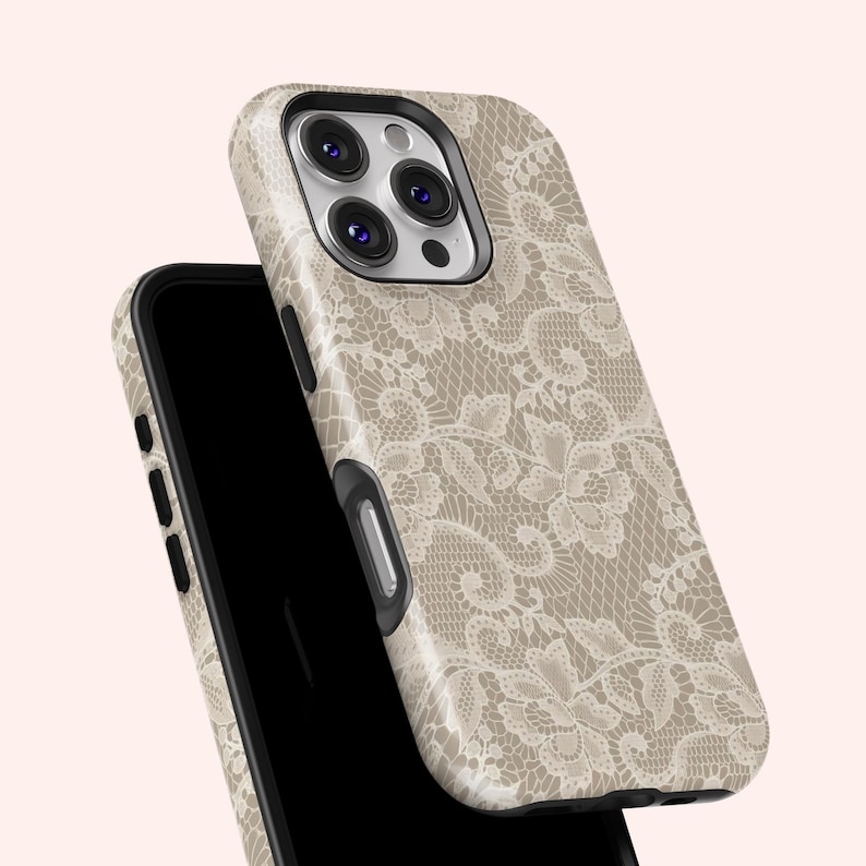 May include: A beige phone case with a delicate, off-white lace pattern. The case is shown on top of a black smartphone, with the camera lenses visible. The design is a floral lace overlay.