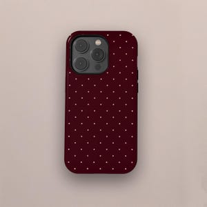 May include: A burgundy phone case with a repeating pattern of small, evenly spaced white dots. The case has a glossy finish and a camera module with three lenses and a flash.