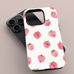 May include: A white phone case featuring a pattern of pink watercolor strawberries with green leaves. The case is on top of a black smartphone with multiple camera lenses.