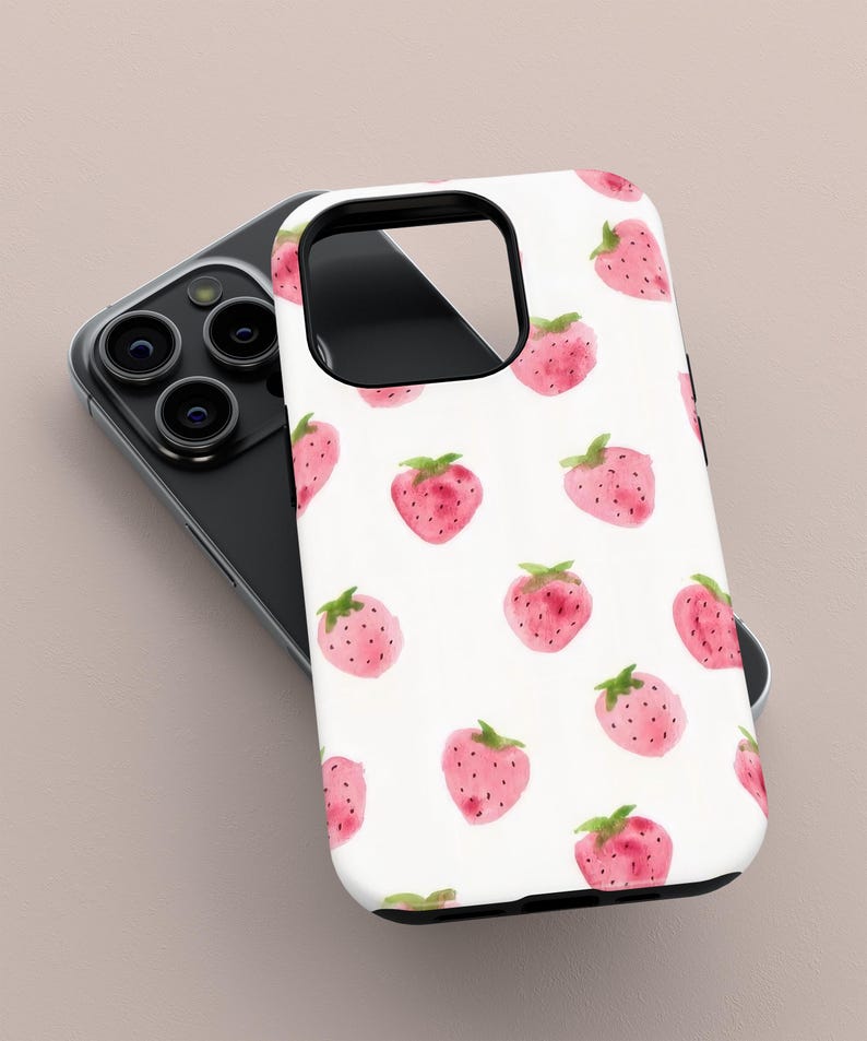 May include: A white phone case featuring a pattern of pink watercolor strawberries with green leaves. The case is on top of a black smartphone with multiple camera lenses.