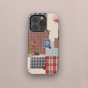 Op de afbeelding: Decoratieve telefoonhoes met een patchwork-ontwerp. Het heeft ruitpatronen, sterren en bloemmotieven in rood, blauw en wit. Een kleine illustratie van een slapend dier en een hart zijn ook aanwezig.