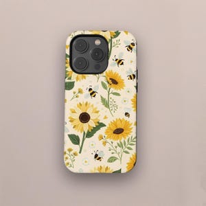 Könnte beinhalten: Eine Handyhülle mit einem sich wiederholenden Muster aus gelben Sonnenblumen, Bienen und kleinen weißen Blumen auf cremefarbenem Hintergrund. Die Hülle hat eine abgerundete Form und einen Kameraausschnitt.