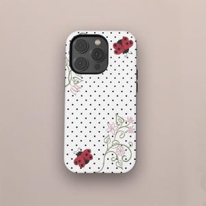 May include: White phone case with a black polka dot pattern and red ladybug illustrations. The case features floral accents in pink and green. The phone case has a camera cutout and black side buttons.