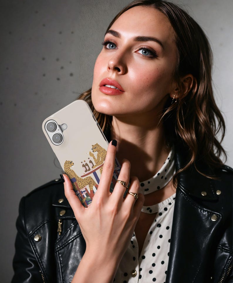 May include: A beige phone case with a design of two cheetahs at a table. The cheetahs are tan with black spots, and the table has a colourful design. The case has a camera cutout and is held by a person.