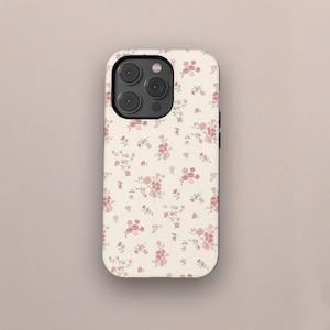 May include: A phone case featuring a floral design. The case has a cream-coloured background adorned with a repeating pattern of small pink roses and green leaves. The phone case has a black camera module.