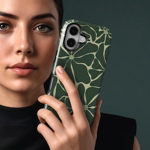 May include: A dark green phone case with a repeating floral design in a lighter green. The case is held in a person's hand, highlighting the pattern and the phone's camera. The case has a shiny finish.