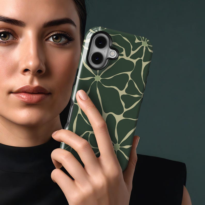 May include: A dark green phone case with a repeating floral design in a lighter green. The case is held in a person's hand, highlighting the pattern and the phone's camera. The case has a shiny finish.