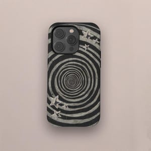 Puede incluir: Funda de teléfono en blanco y negro con un diseño de espiral y detalles de estrellas plateadas. La funda tiene un acabado brillante y un recorte para la cámara. El diseño crea una ilusión óptica.