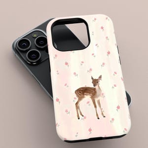 May include: A phone case with a watercolour illustration of a fawn with brown spots and a light pink background. The case is decorated with small pink flowers. The phone case is resting on top of a black phone.