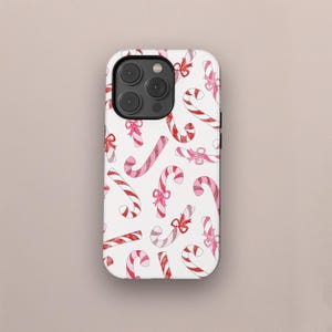 May include: White phone case featuring a repeating pattern of red and pink candy canes with bows. The candy canes have red and pink stripes and are decorated with pink bows. The case has a glossy finish.