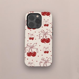 May include: A phone case with a repeating pattern of red cherries tied with bows and small red hearts on a cream background. The case has a camera module with three lenses.