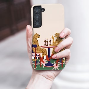 May include: A phone case with a quirky design of two cheetahs at a table with bottles. The cheetahs are wearing boots and sitting on chairs. The case has a light beige background.