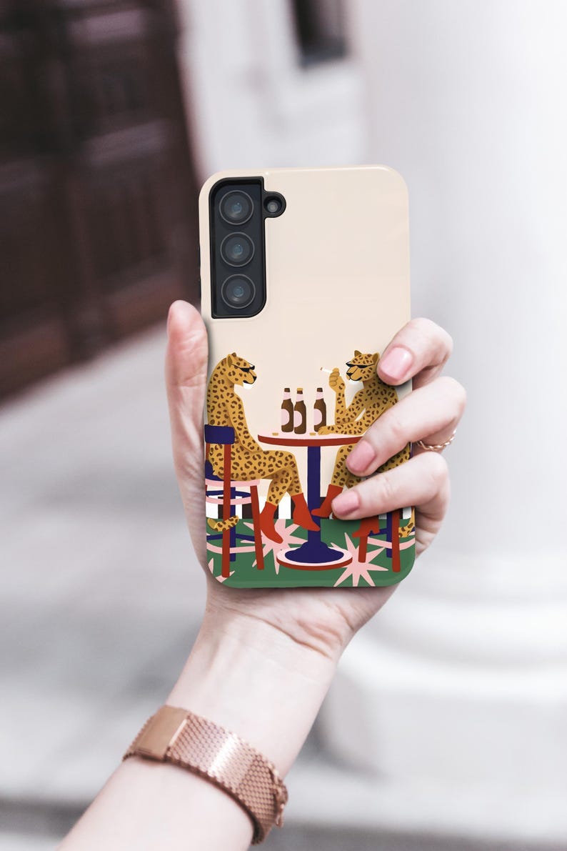 May include: A phone case with a quirky design of two cheetahs at a table with bottles. The cheetahs are wearing boots and sitting on chairs. The case has a light beige background.