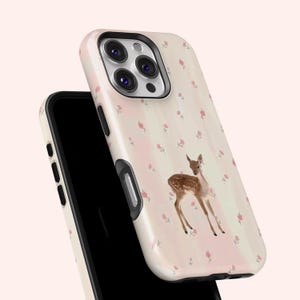 May include: A phone case with a fawn illustration. The case has a cream background with vertical pink stripes and small pink floral accents. The fawn is brown with white spots.
