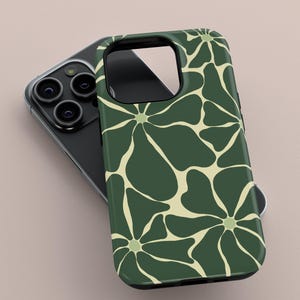 May include: A dark green phone case featuring a cream floral design. The case is placed on a black phone with multiple camera lenses. The floral pattern consists of large, stylized flowers, giving a retro feel. The case is made of a glossy material.