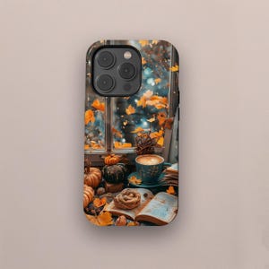 Op de afbeelding: Een telefoonhoesje met een herfstontwerp. Het toont een raam met vallende oranje bladeren, pompoenen, een kopje koffie en een open boek. De hoes heeft een zwarte rand en een glanzende afwerking, perfect voor de herfst.